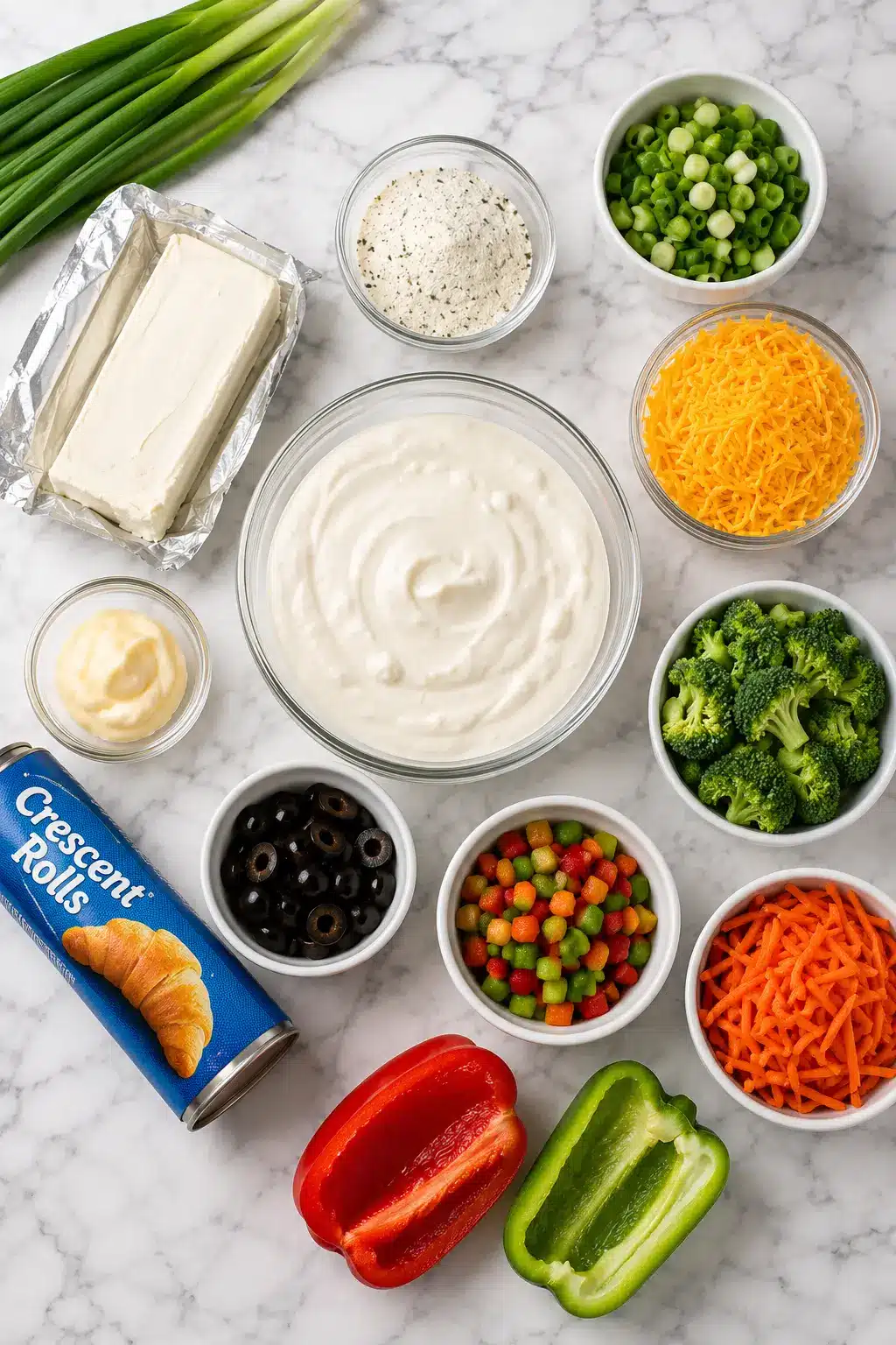 Crescent Roll Veggie Pizza Ingredients for Crescent Roll Veggie Pizza including crescent roll dough, cream cheese, ranch seasoning, mayonnaise, sour cream, shredded cheddar cheese, broccoli, carrots, bell peppers, green onions, black olives, and cucumber arranged on a white marble countertop.