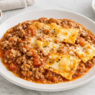 Crockpot Ravioli Lasagna served hot with layers of ravioli, meat sauce, and melted cheese on a white plate