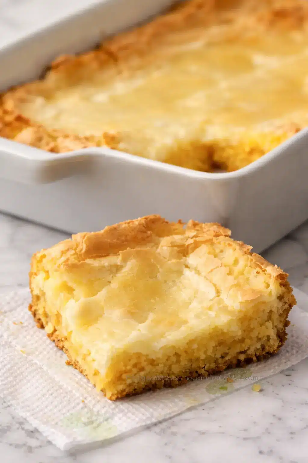 Gluten-Free French Butter Cake 1 A slice of Gluten-Free French Butter Cake with a creamy cream cheese topping and buttery golden base, served on a white marble surface