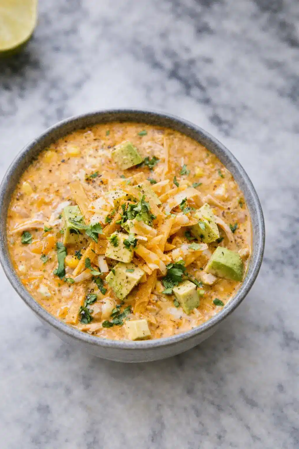 Healthy high protein white chicken chili in a bowl with shredded chicken, white beans, avocado, and cilantro on a marble surface
