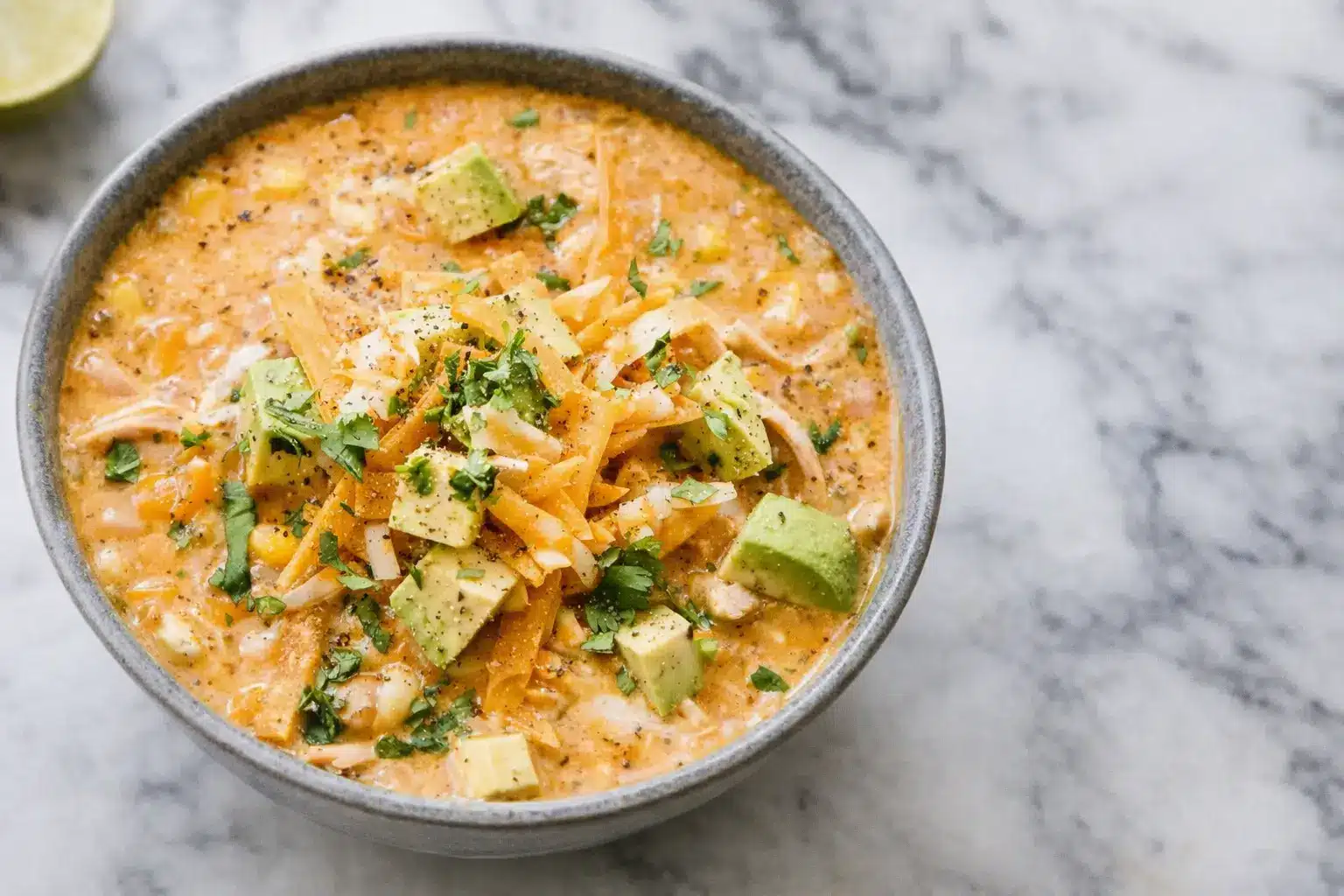 Healthy high protein white chicken chili served in a bowl with shredded chicken, beans, and fresh cilantro on a marble surface