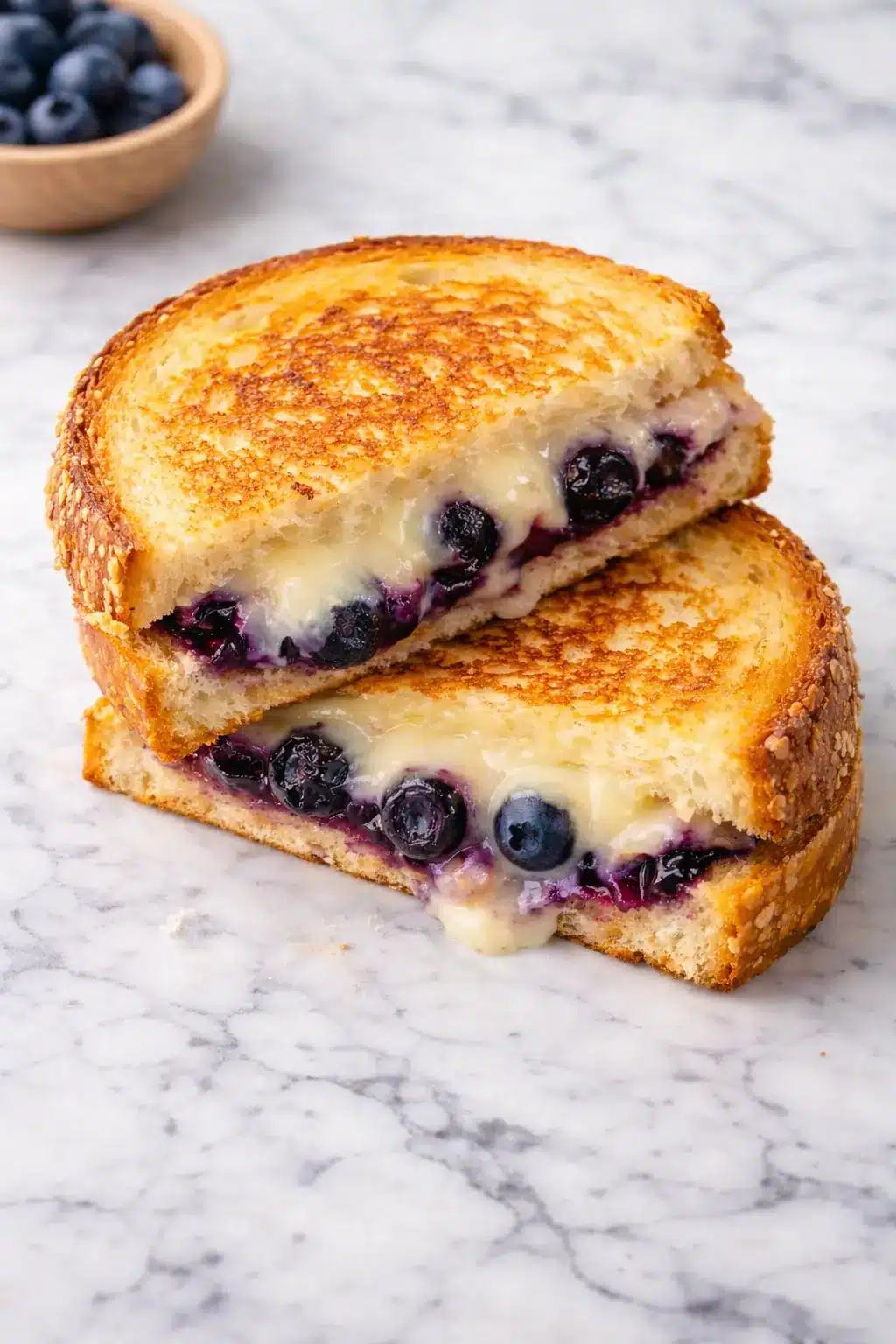Vertical photorealistic image of a juicy blueberry grilled cheese sandwich with melted cheese and whole blueberries on golden toasted bread, styled on white marble background
