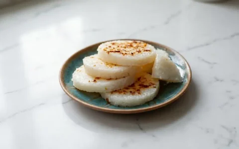 Photorealistic South Asian rice cake, freshly cooked and naturally plated on white marble, ready to serve with a home kitchen feel.