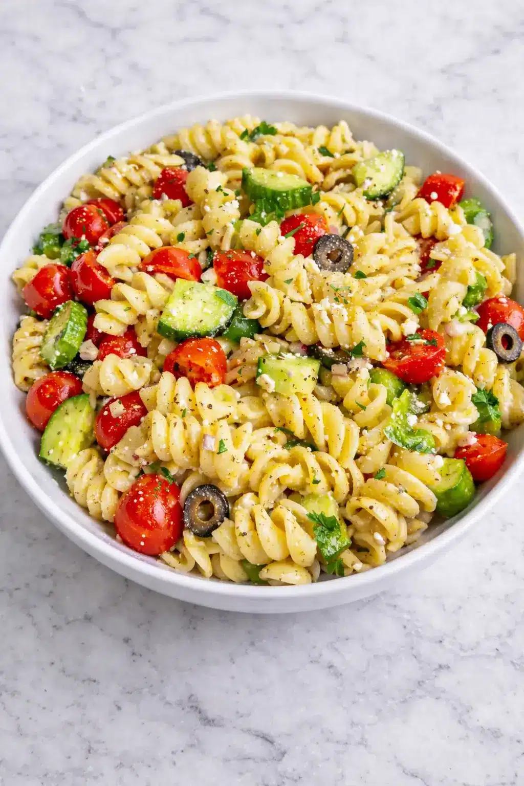 The Best Pasta Salad with Italian Dressing in a white bowl with rotini pasta, cherry tomatoes, cucumber, olives, and feta cheese