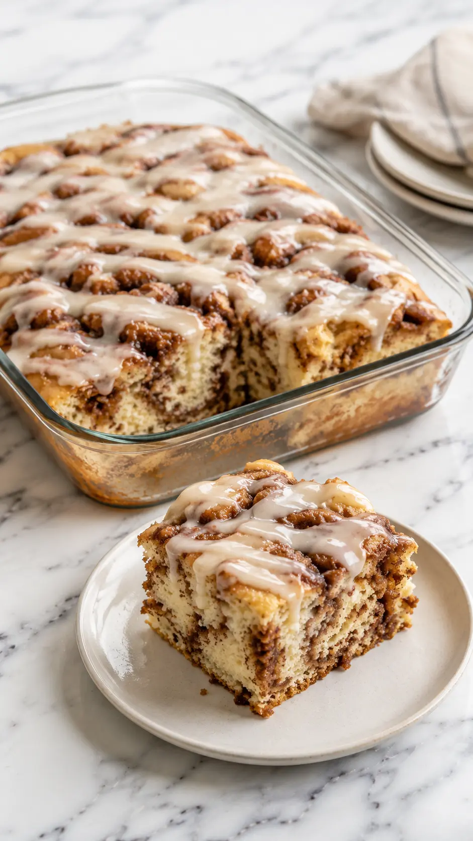 Cinnabon Cinnamon Roll Cake Freshly baked Cinnabon Cinnamon Roll Cake with cinnamon swirls and vanilla glaze on a white plate.