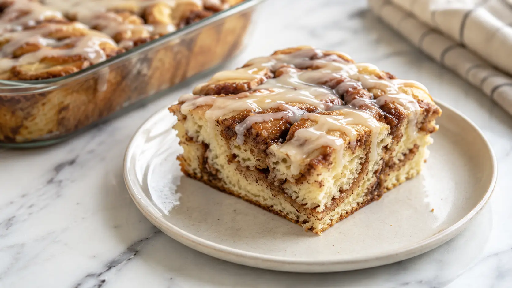 Cinnabon Cinnamon Roll Cake Freshly baked Cinnabon Cinnamon Roll Cake with cinnamon swirls and vanilla glaze on a white plate.