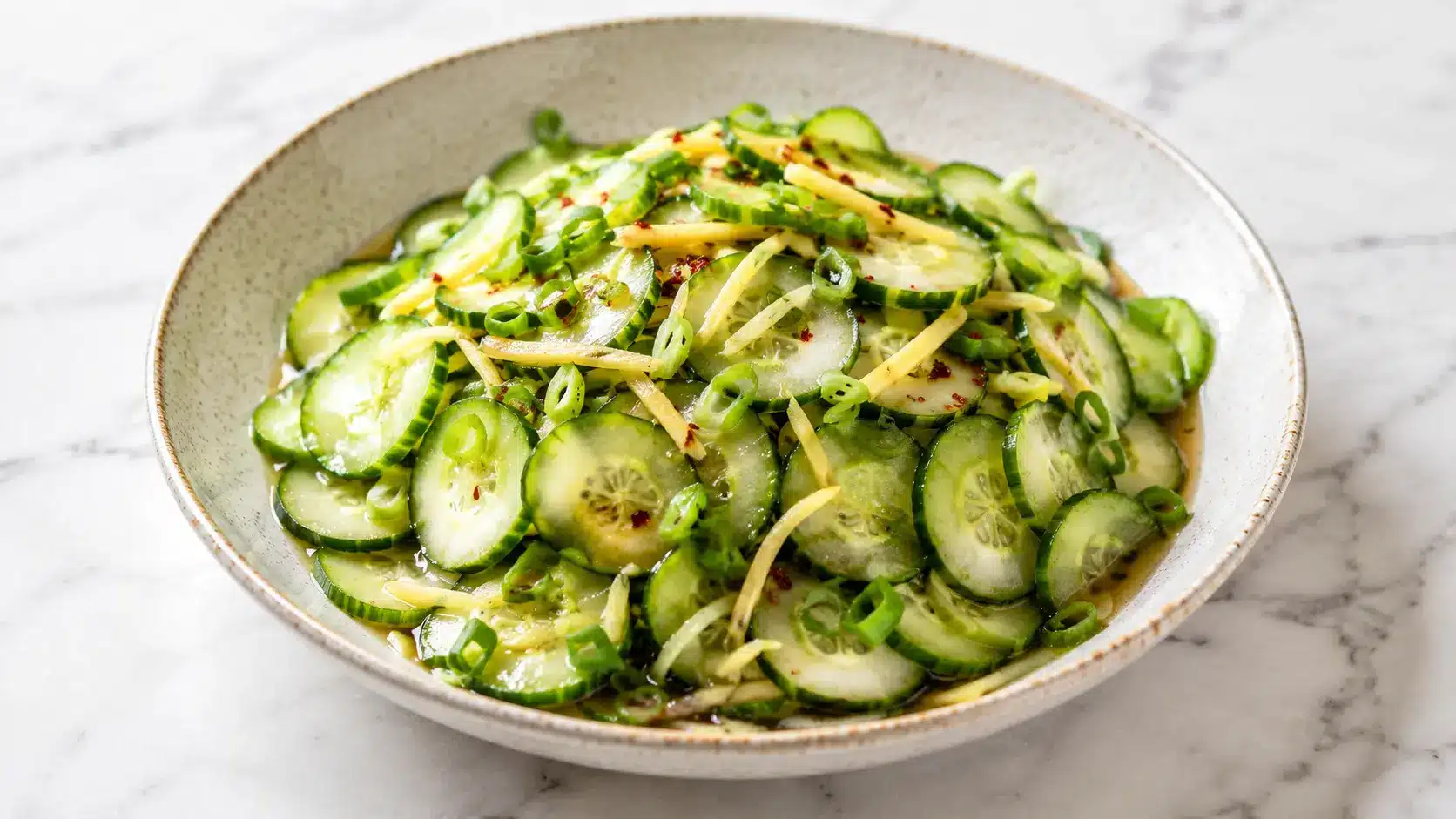 Crispy Cucumber Ginger Salad served in a ceramic bowl with thin cucumber slices, fresh ginger, scallions, and a light marinade on a white marble surface.