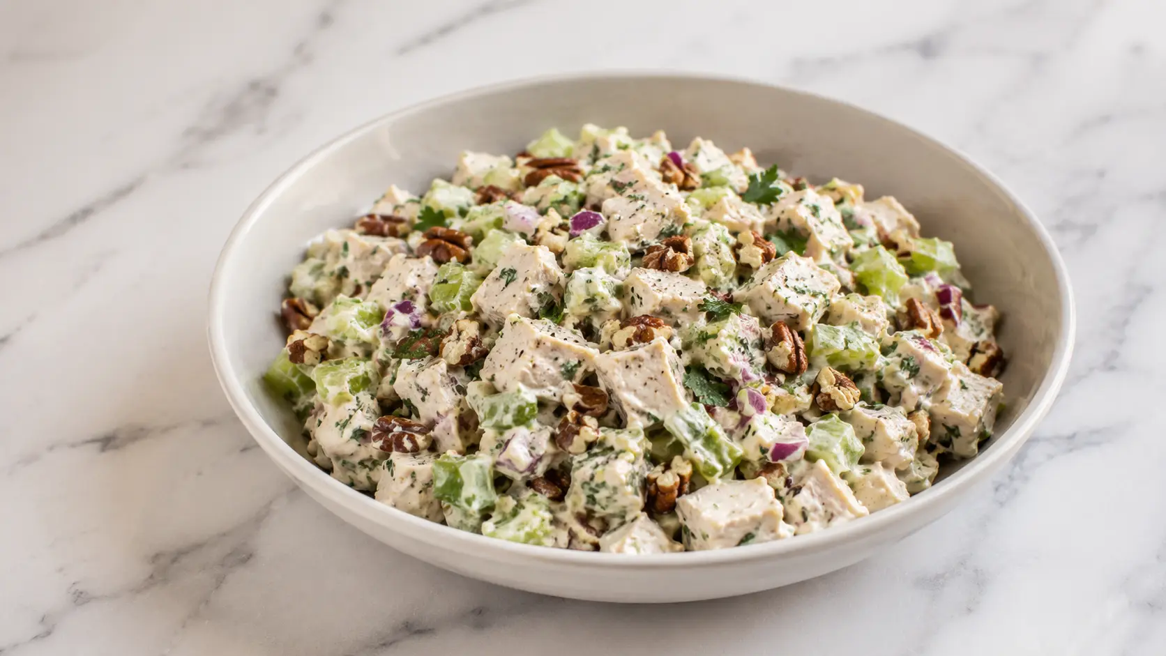 Healthy Chopped Southwest Chicken Salad served in a bowl with cooked chicken, celery, toasted pecans, fresh herbs, and a creamy yogurt dressing on a white marble surface.